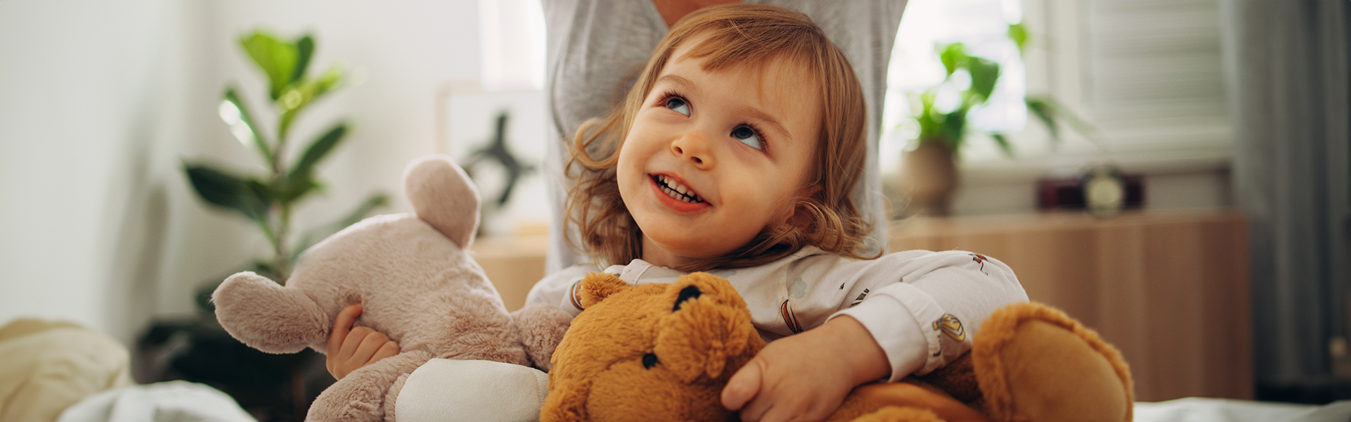 toddler girl holding a couple of teddy bears while smiling