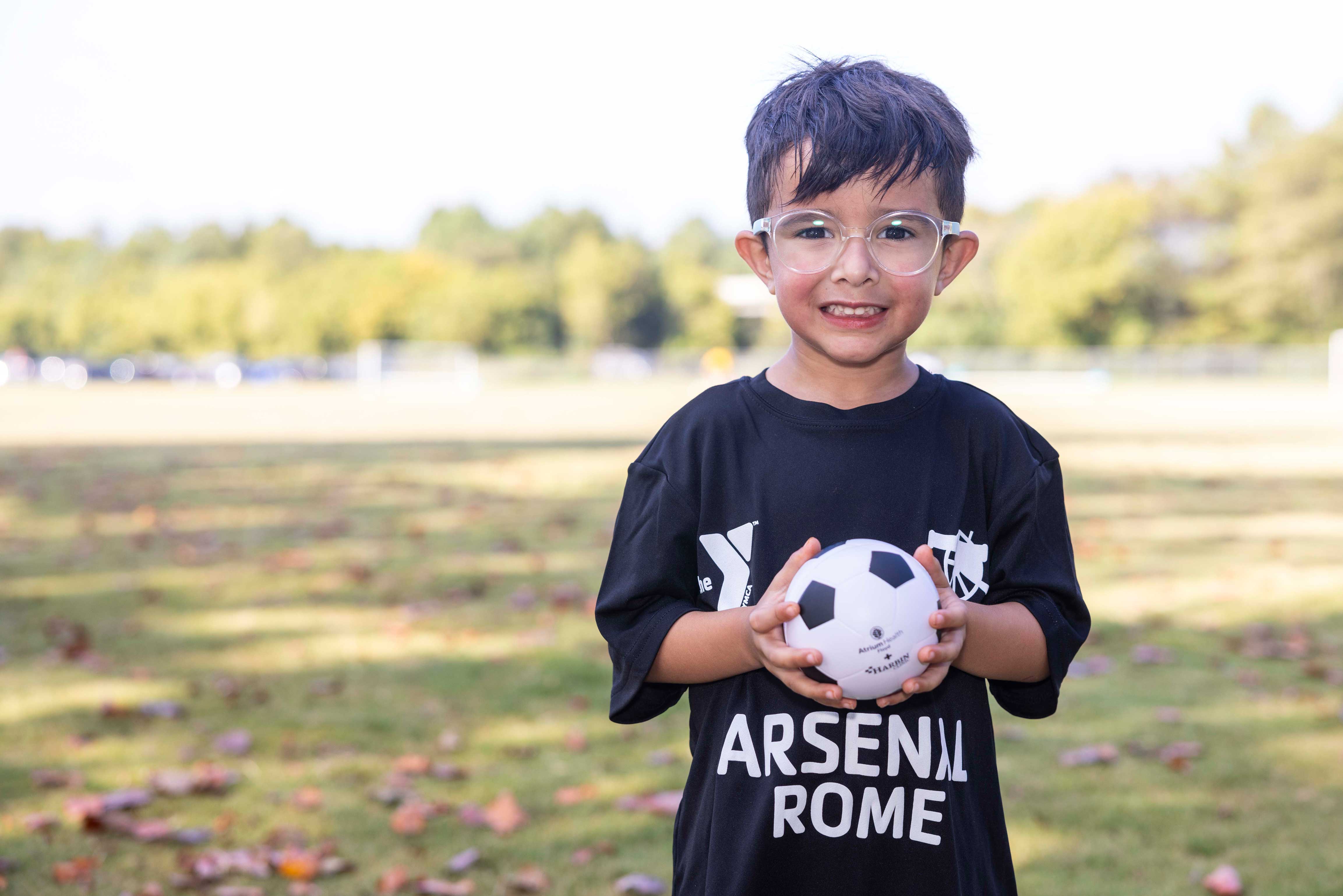 young boy wearing glasses holding a mini-soccer ball