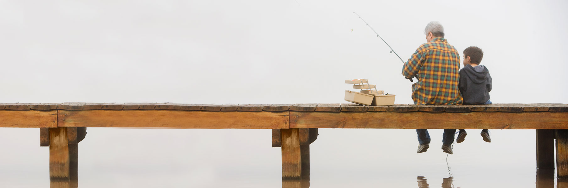 Man and young boy sitting on dock while fishing