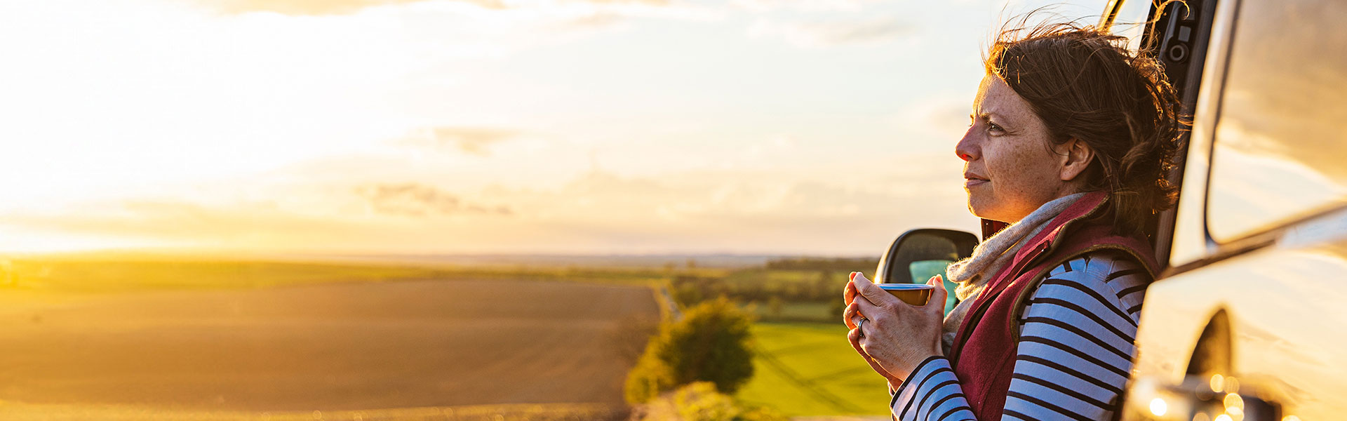 woman standing outside holding a cup of coffee and looking at a sunrise